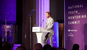 Prince Harry standing at a lectern on stage at Banking Hall